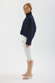 Side view of Model wearing Blue Jay jacket in Indigo with white cropped pants and sandals